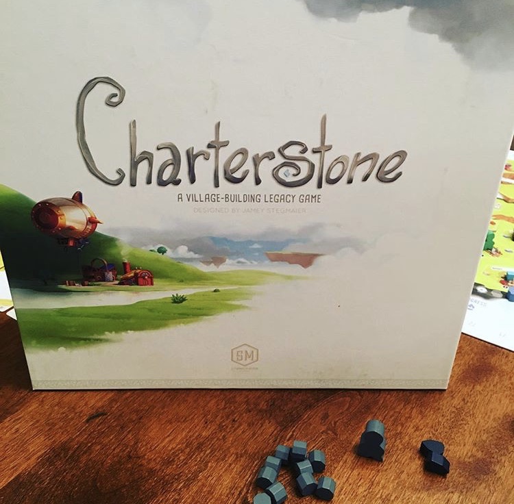 Box of the Charterstone board game, with some of the game pieces in front. 